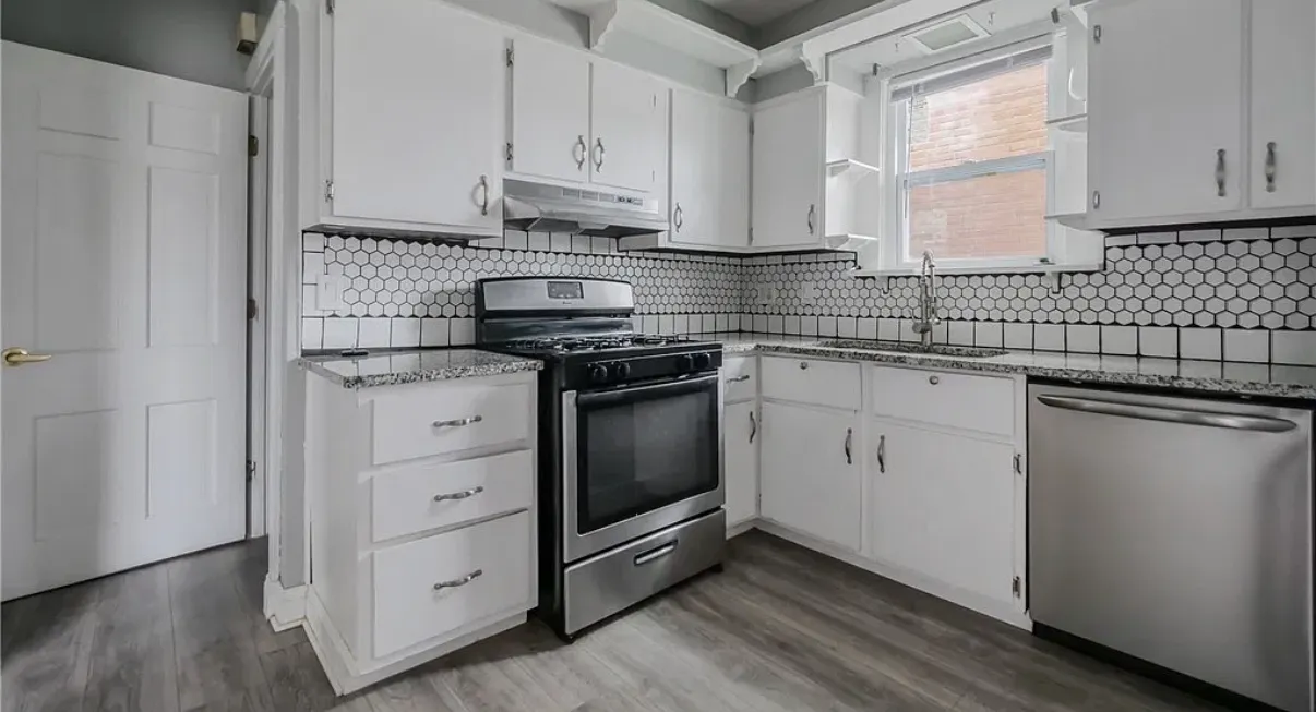 Kitchen with white cabinets, a hexagonal tile backsplash, granite counters and a stainless gas range
